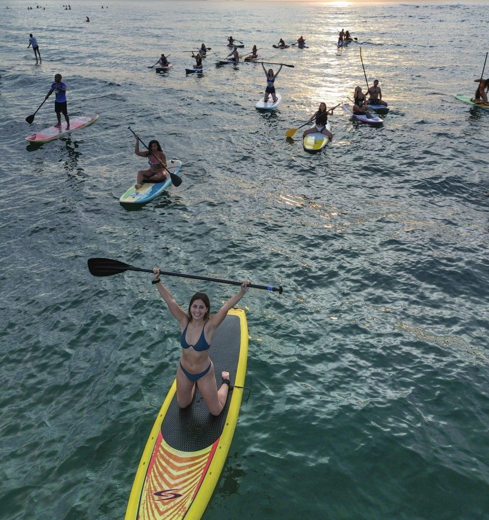 A group enjoys paddleboarding in the ocean at sunset, highlighting leisure and water sports.